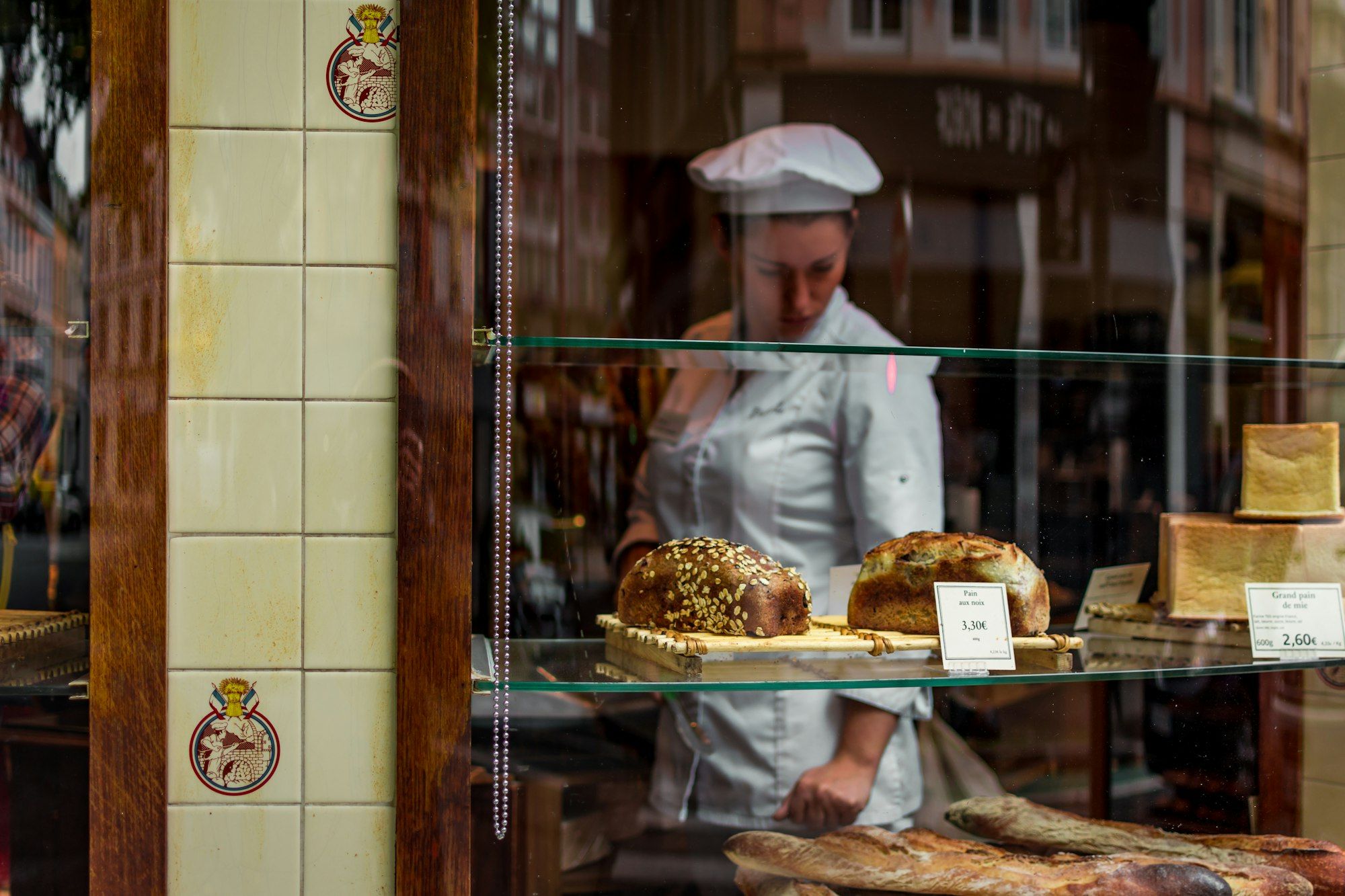Baker working behind the glass shopfront of a bakery stocked with fresh bread