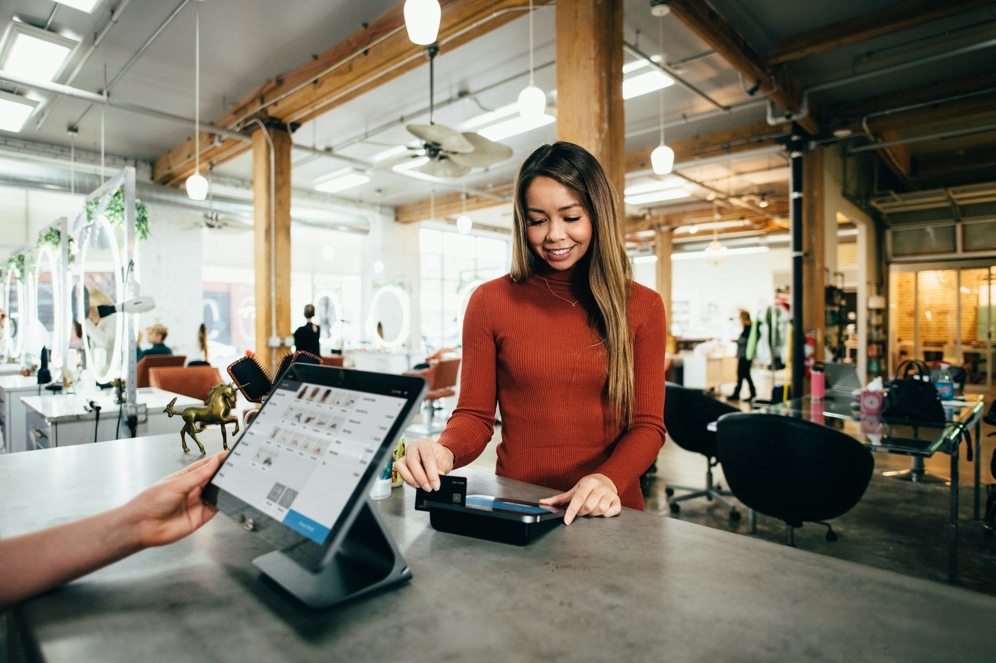 Woman in a rust-coloured sweater paying by card at a shop checkout counter