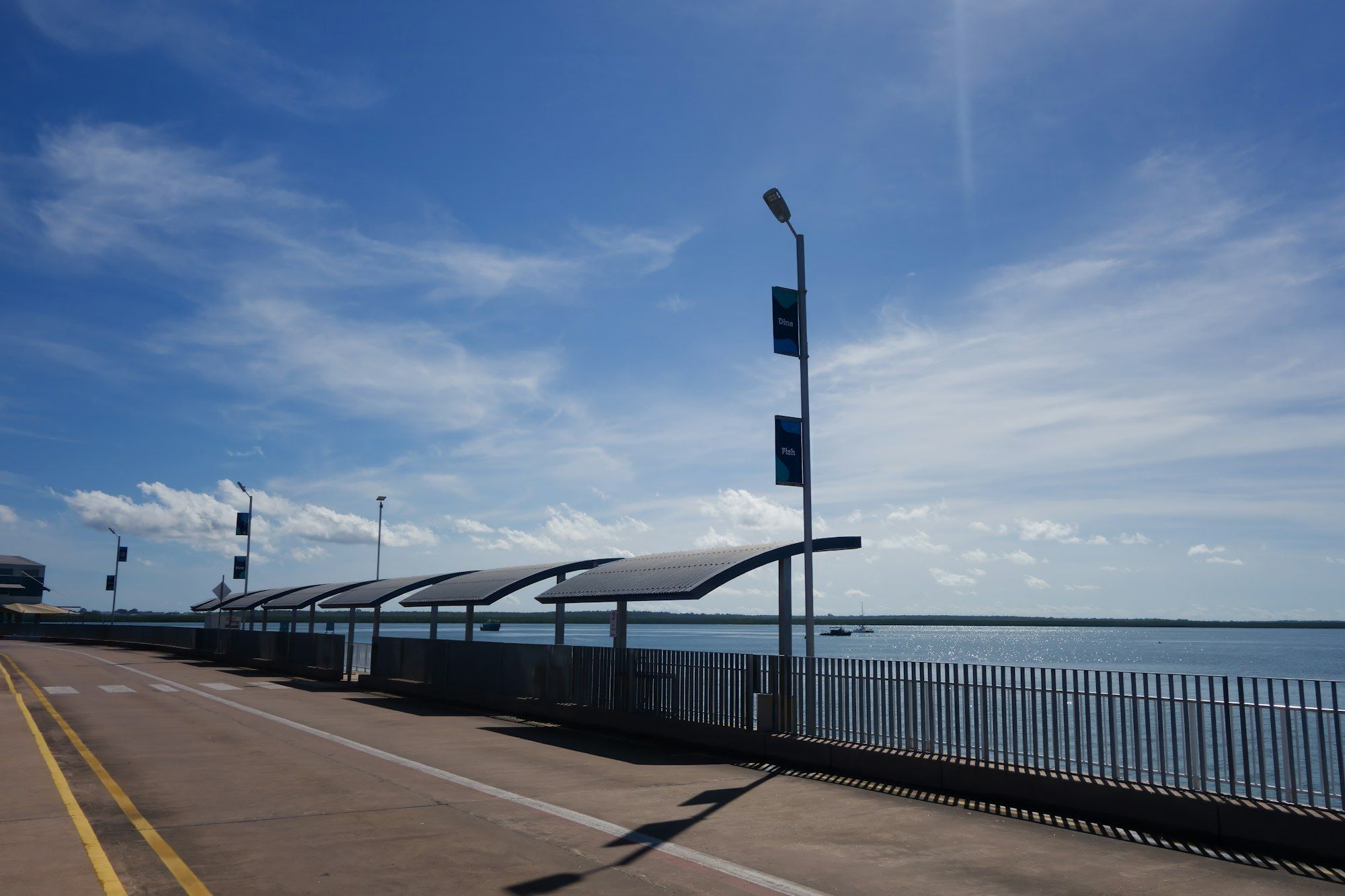 Darwin waterfront path with shade shelters and boats under a bright blue sky