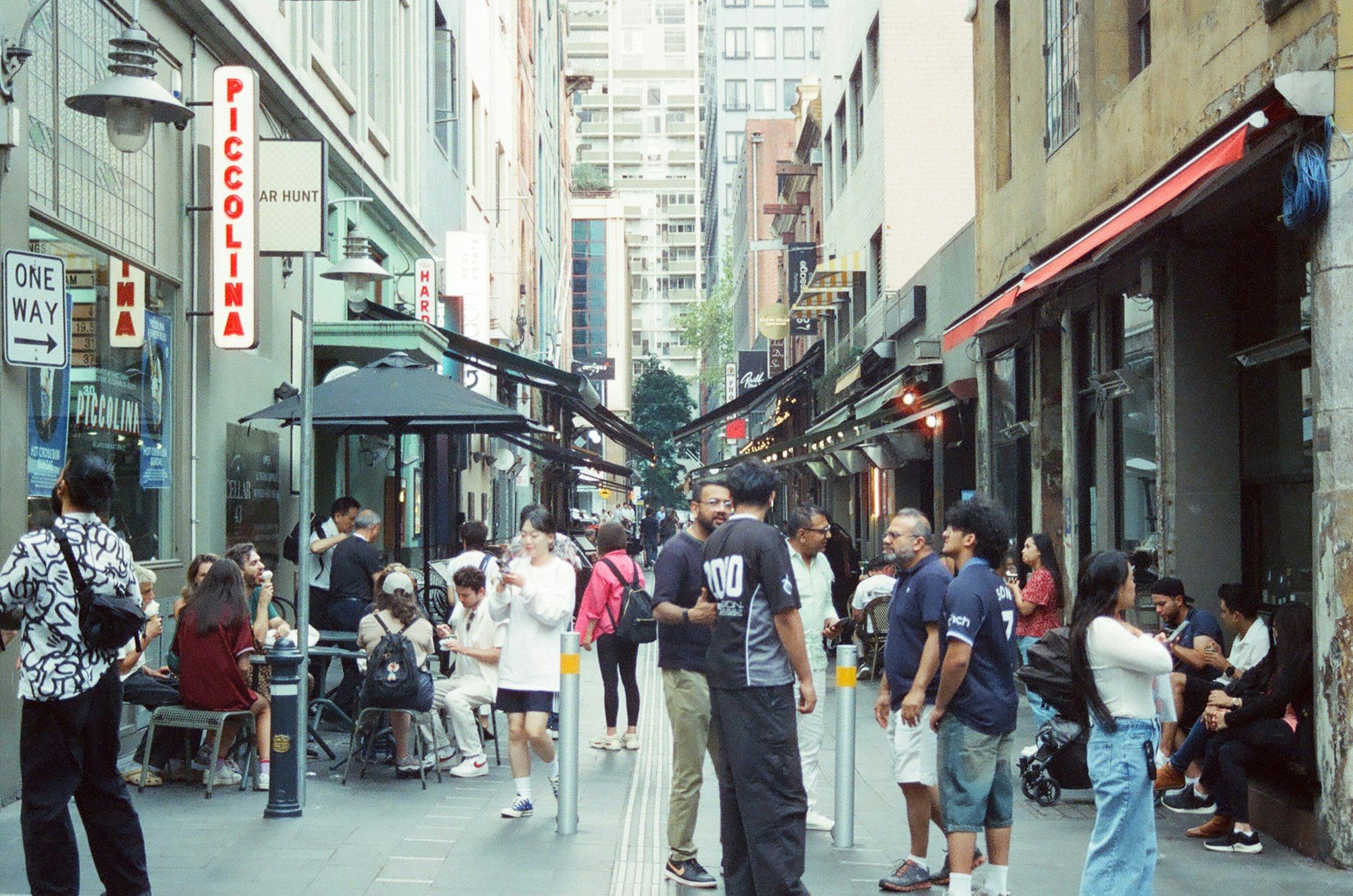 People gathered at outdoor cafe tables in a narrow Melbourne laneway lined with shops